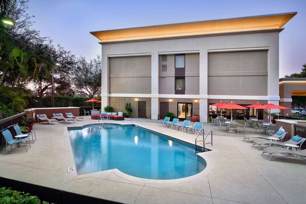 Exterior view of the Hampton Inn Naples I-75, featuring a well-lit entrance, palm trees, and a welcoming facade under a clear blue sky.