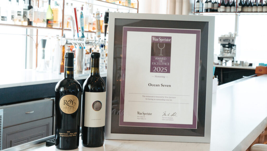 Wine bottles displayed beside the 2025 Wine Spectator Award of Excellence earned by Ocean Seven at The Hiatus Clearwater Beach.